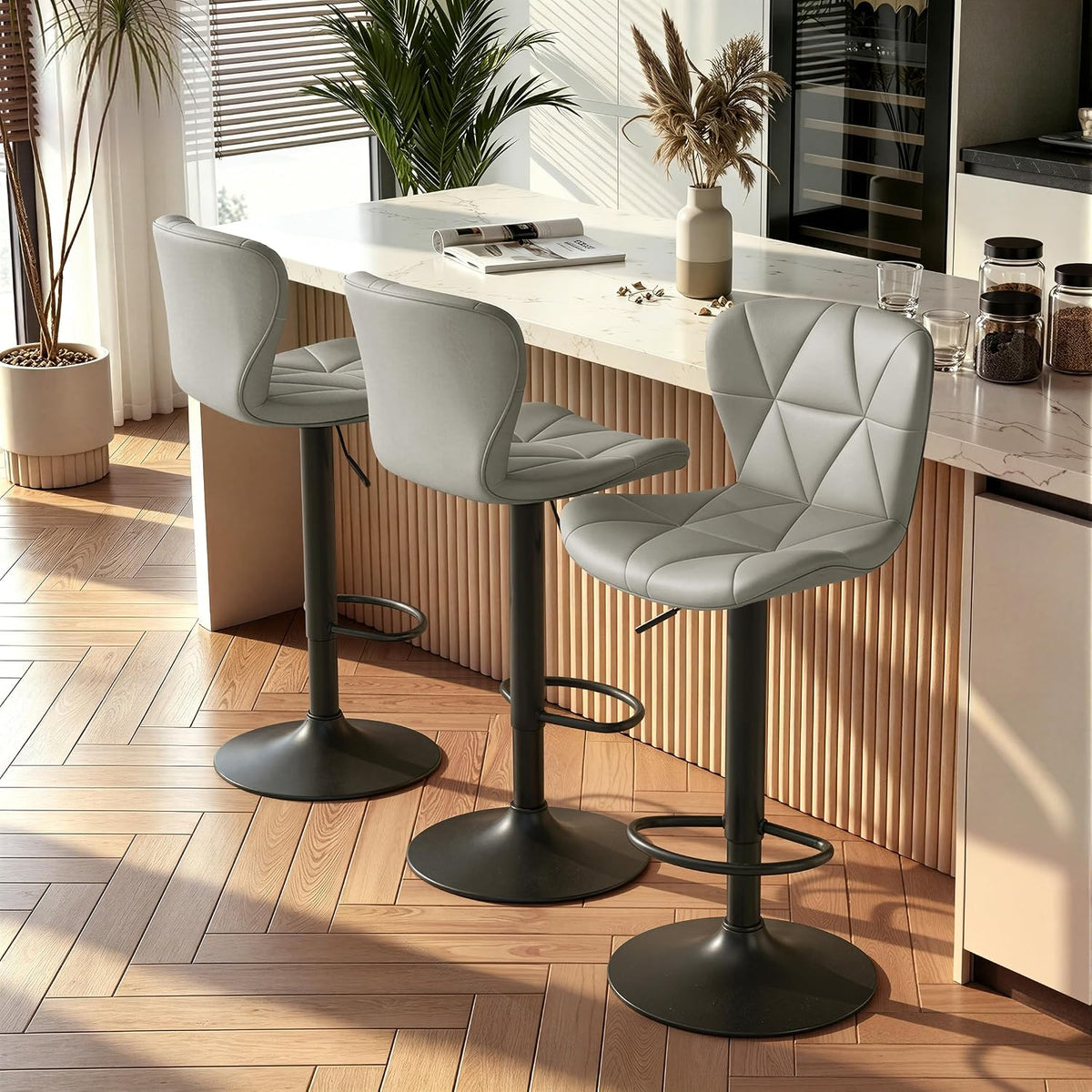 Three light-gray bar stools at a fluted-front island with herringbone wood floor and sunlight patterns