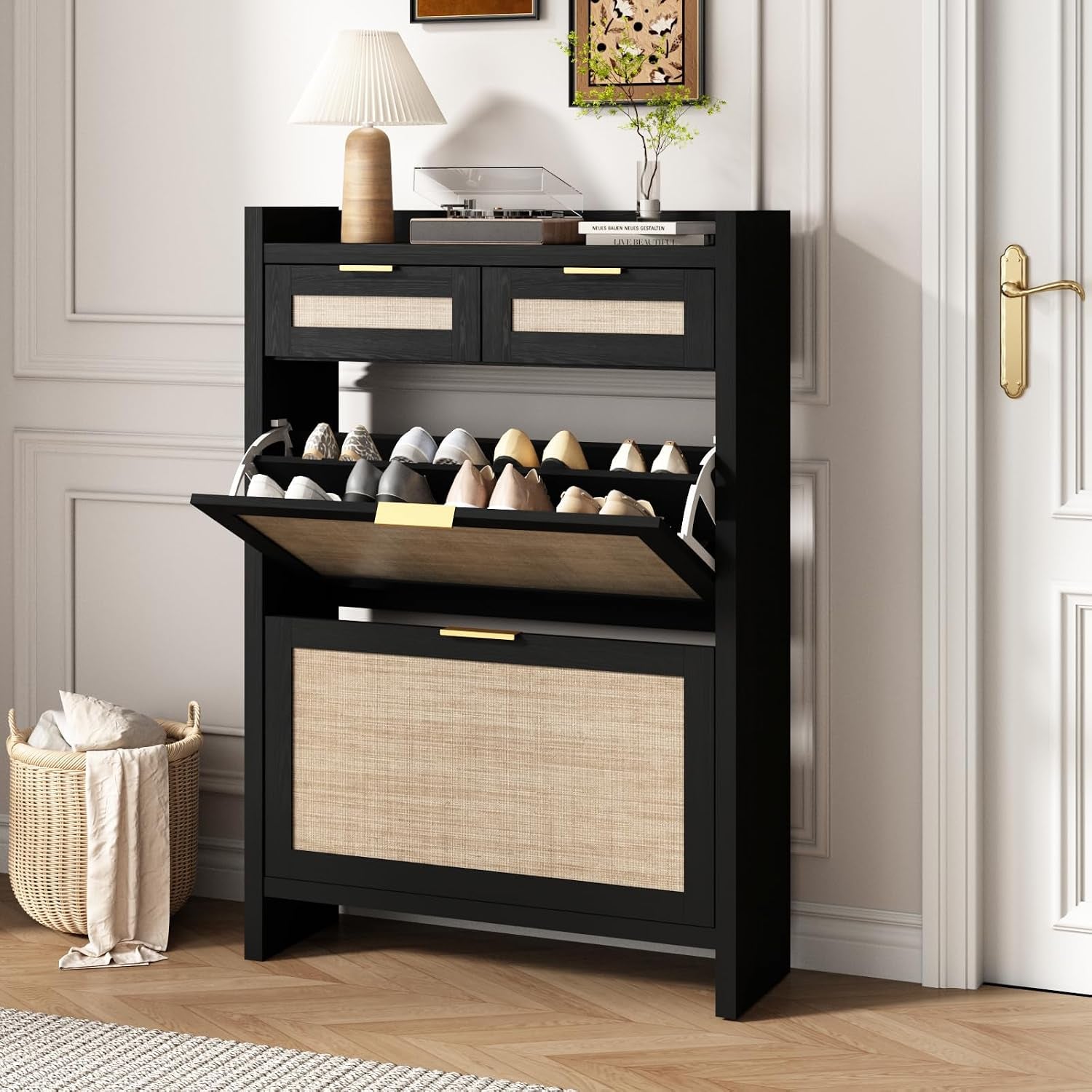 Black rattan-front shoe cabinet with an open top flip drawer, lamp on top and a basket on the floor beside it.