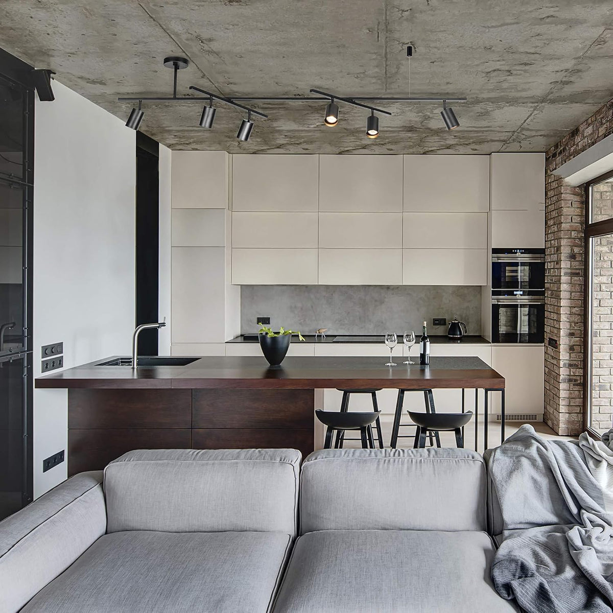 Matte black 6-light track fixture mounted on a concrete ceiling above an open-plan kitchen