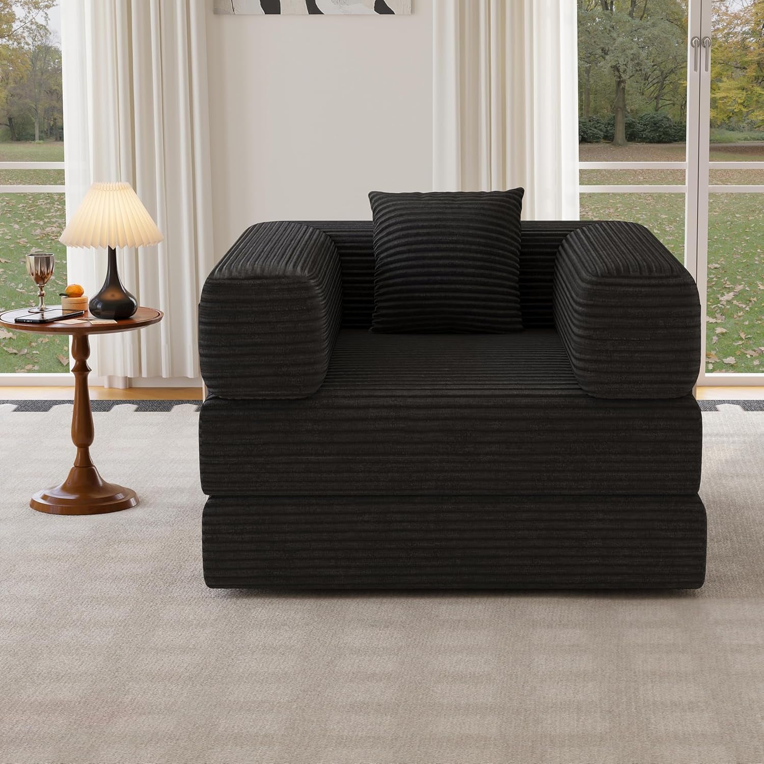 Front-facing black corduroy two-seat convertible floor sofa placed before tall windows and side table.