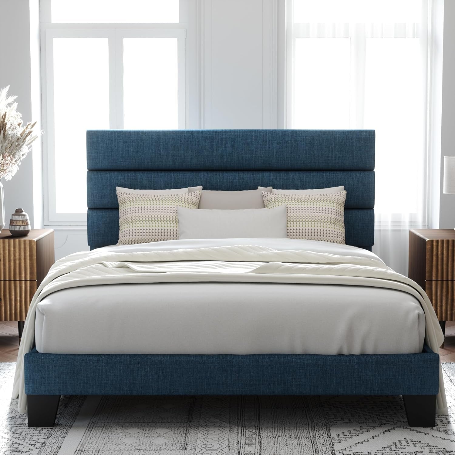 Front room view of a navy blue bed with white bedding and a three-section padded headboard.