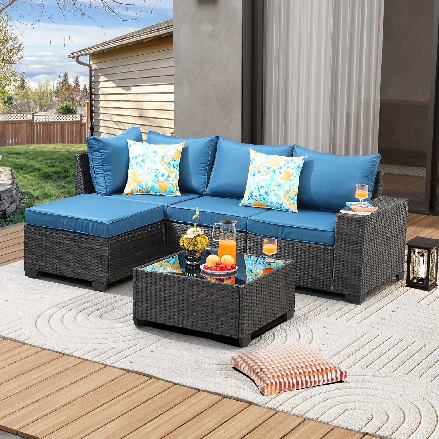 Patio scene with blue-cushioned sectional, matching ottoman and woven glass-top coffee table.