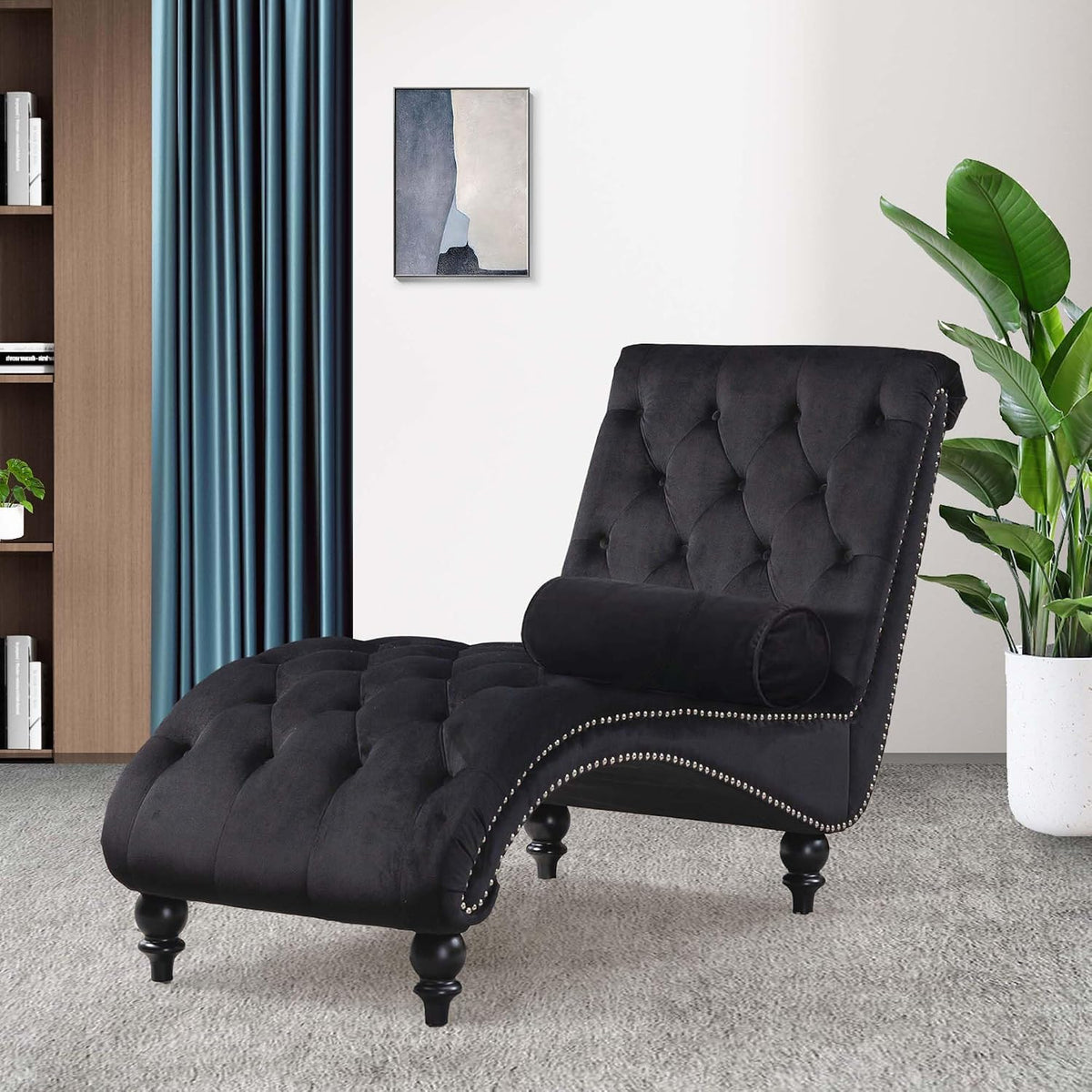 Black tufted chaise angled right with bolster pillow, bookshelf and teal curtain in the background