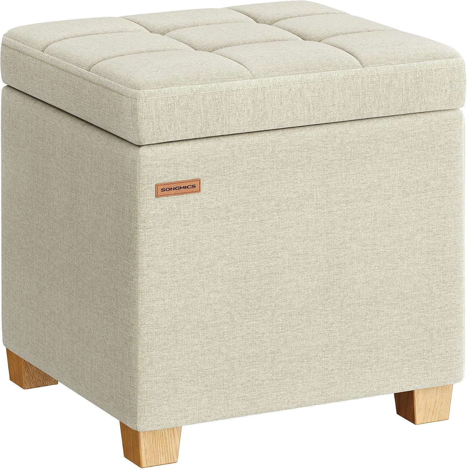 Three-quarter view of a square tufted-top fabric storage ottoman in light beige on short wooden legs.