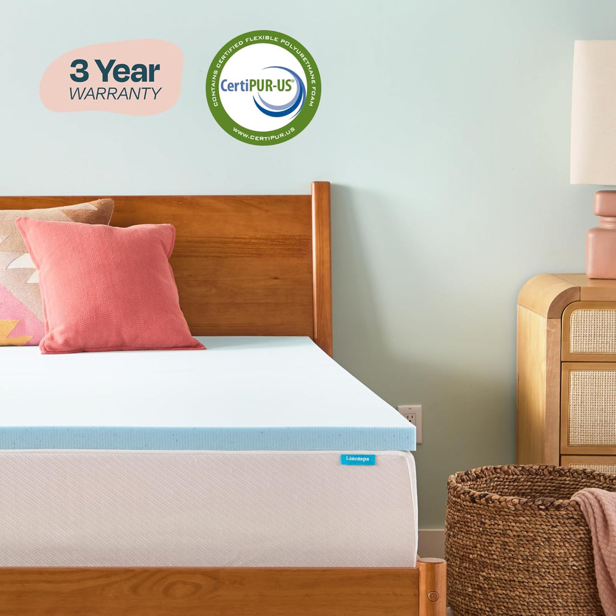 Light-blue foam mattress topper laid flat on a white mattress in a bedroom with wooden headboard and bedside basket.