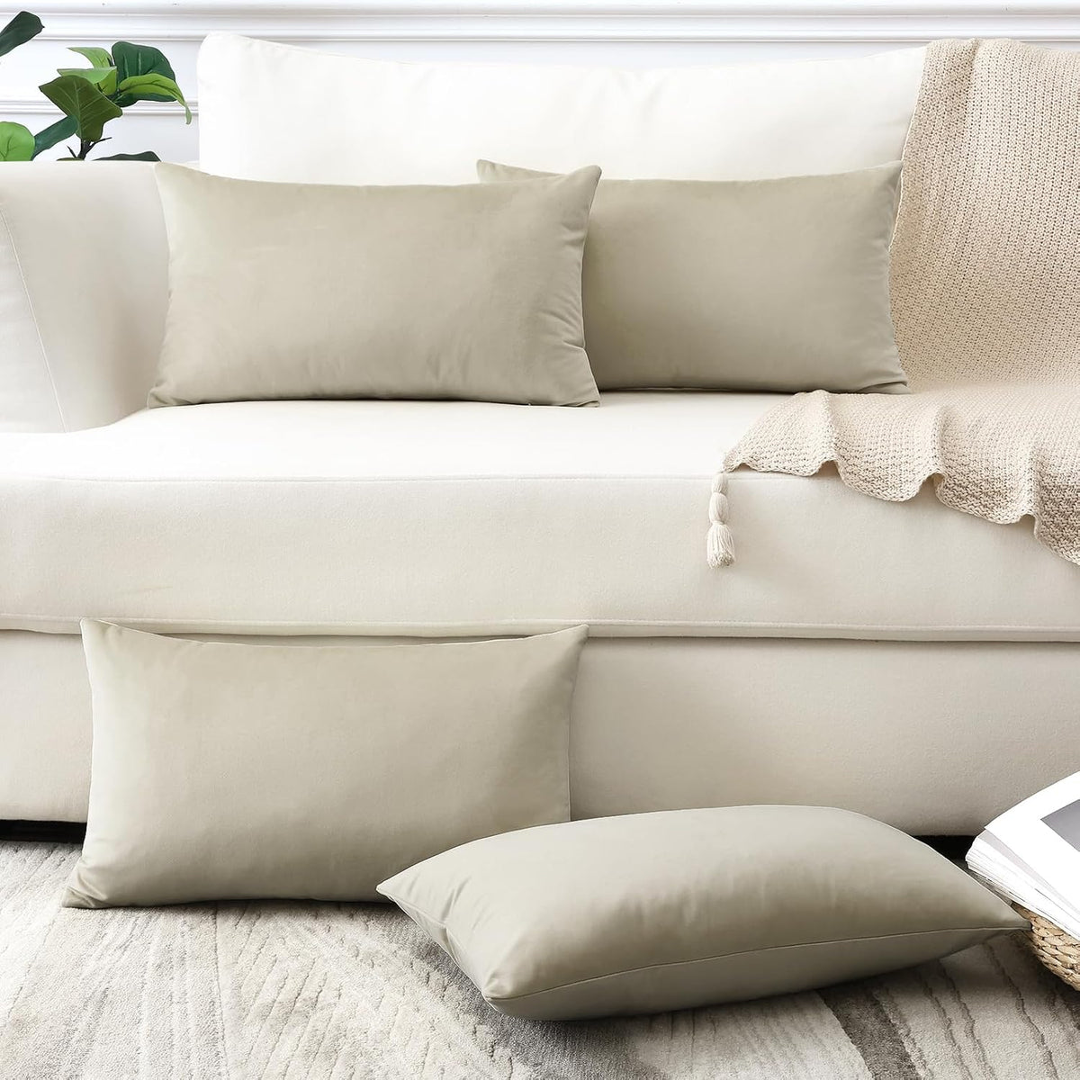 Two taupe rectangular pillow covers on a cream sofa with matching pillows on the floor and a knit throw