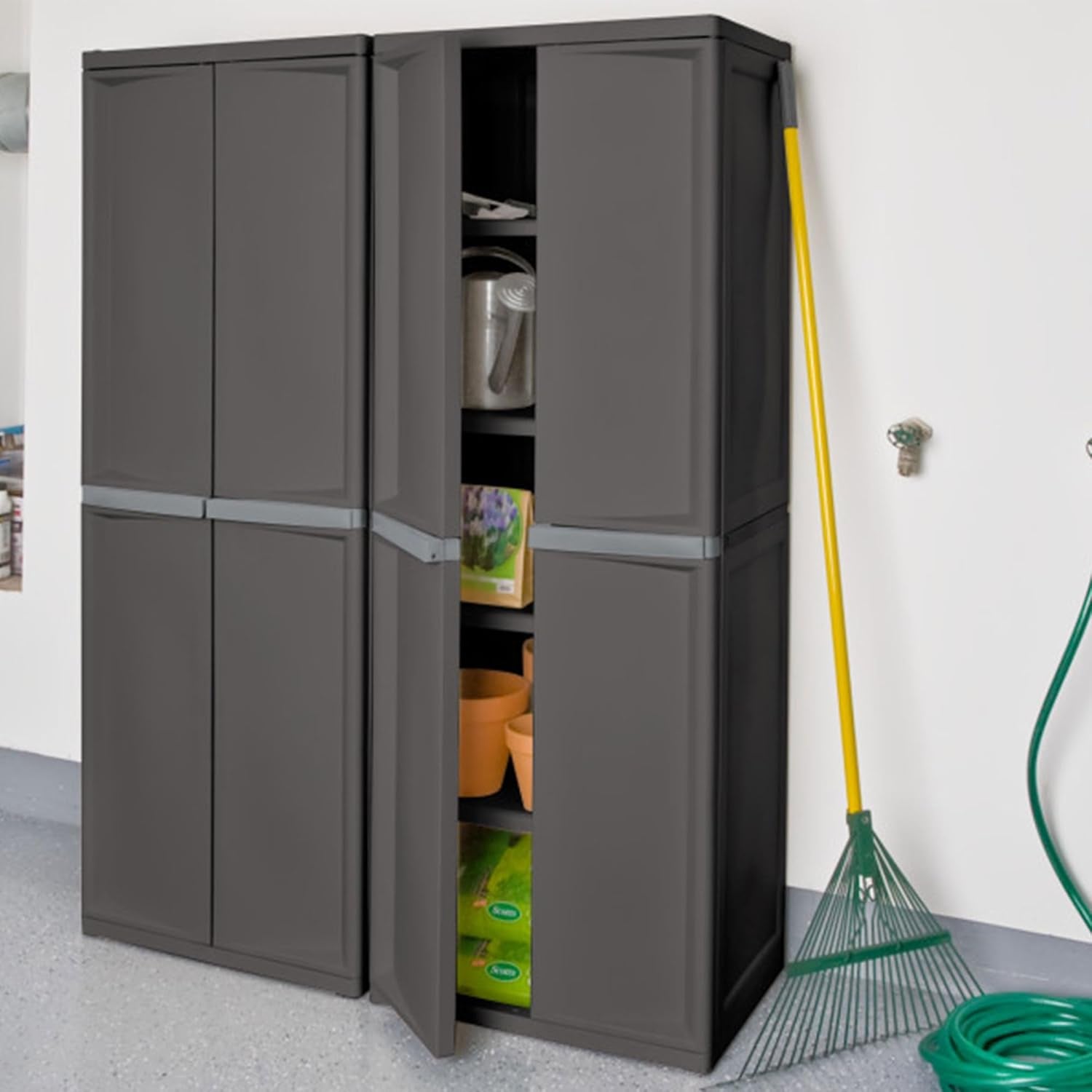 Two dark gray tall storage cabinets side by side in a garage setting with one door open showing gardening items on shelves.