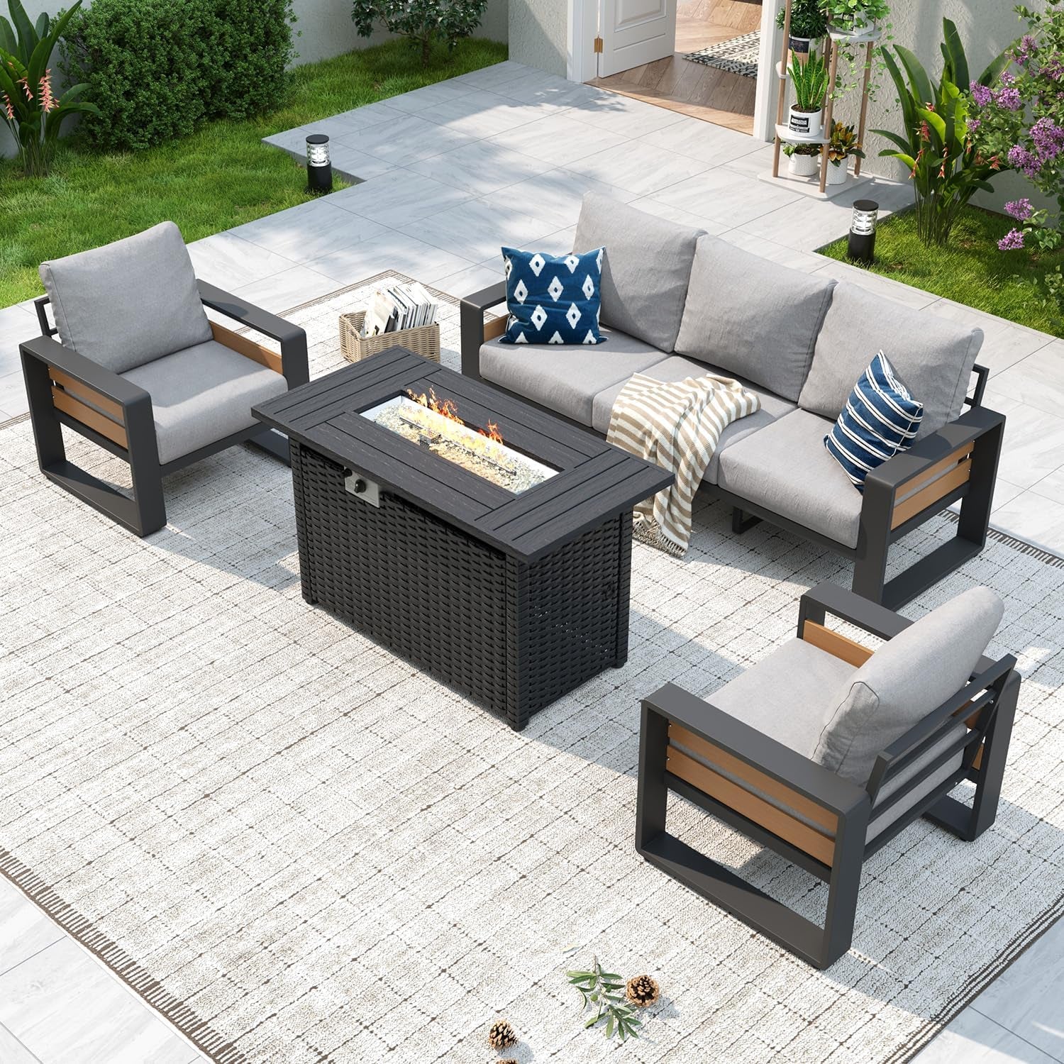 Outdoor sectional with light-gray cushions and dark frames facing a rectangular dark fire-pit table with visible flames.