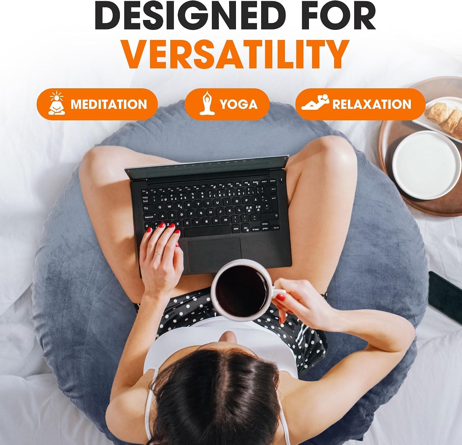 Top-down view of a person seated on a blue round floor pillow using a laptop and holding a cup of coffee