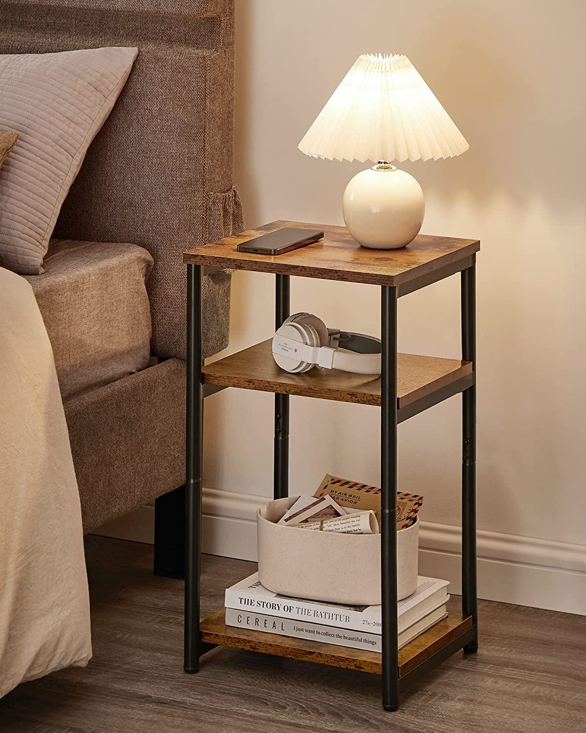 Side table used as a bedside table with lamp on top and storage items on middle and bottom shelves