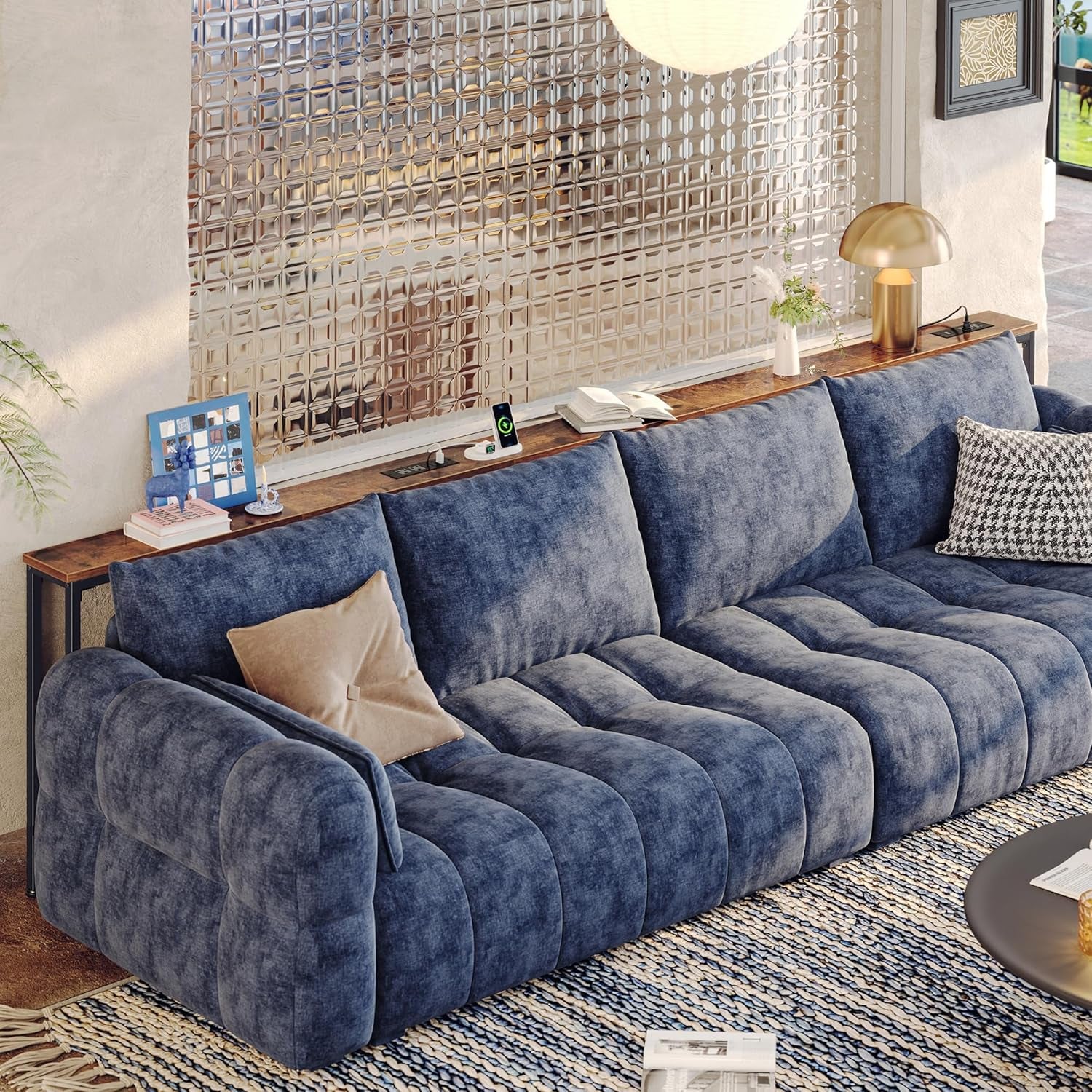Long rustic wood sofa table running behind a blue sectional sofa with lamp, books, and a charging puck on top.
