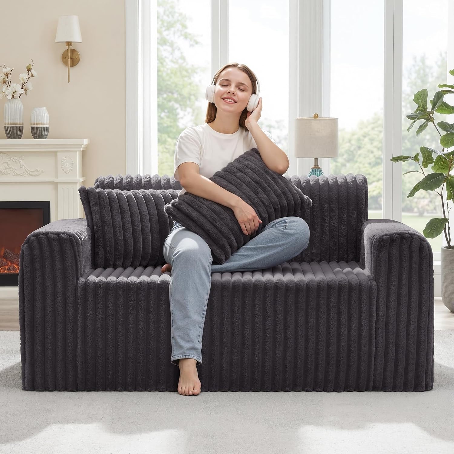 Woman sitting cross-legged on a dark gray ribbed floor sofa, hugging a matching pillow.