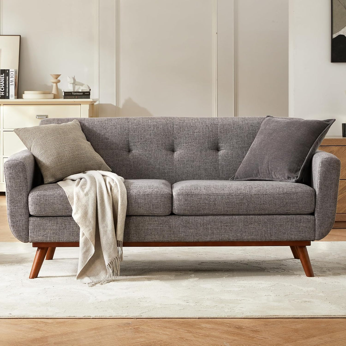 Front-facing gray loveseat with tufted back, two seat cushions, throw and pillows on a rug.