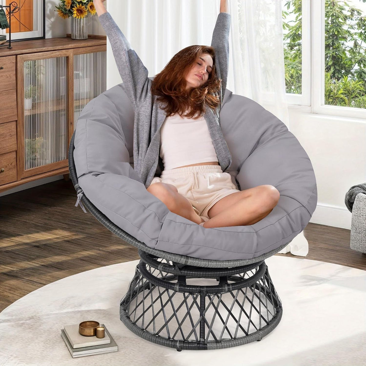 Woman relaxing and stretching while seated cross-legged in a light gray-cushioned papasan chair.