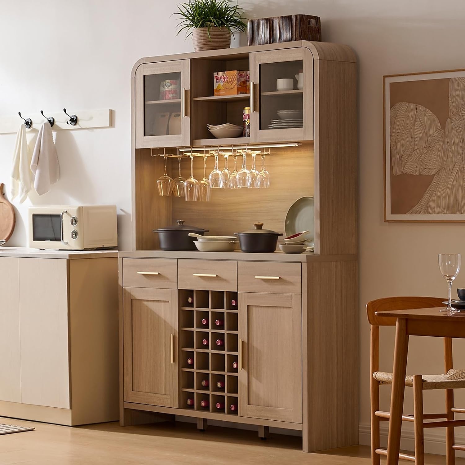 Gray oak pantry and buffet staged in a kitchen with hanging wine glasses, cookware on counter and a small microwave nearby