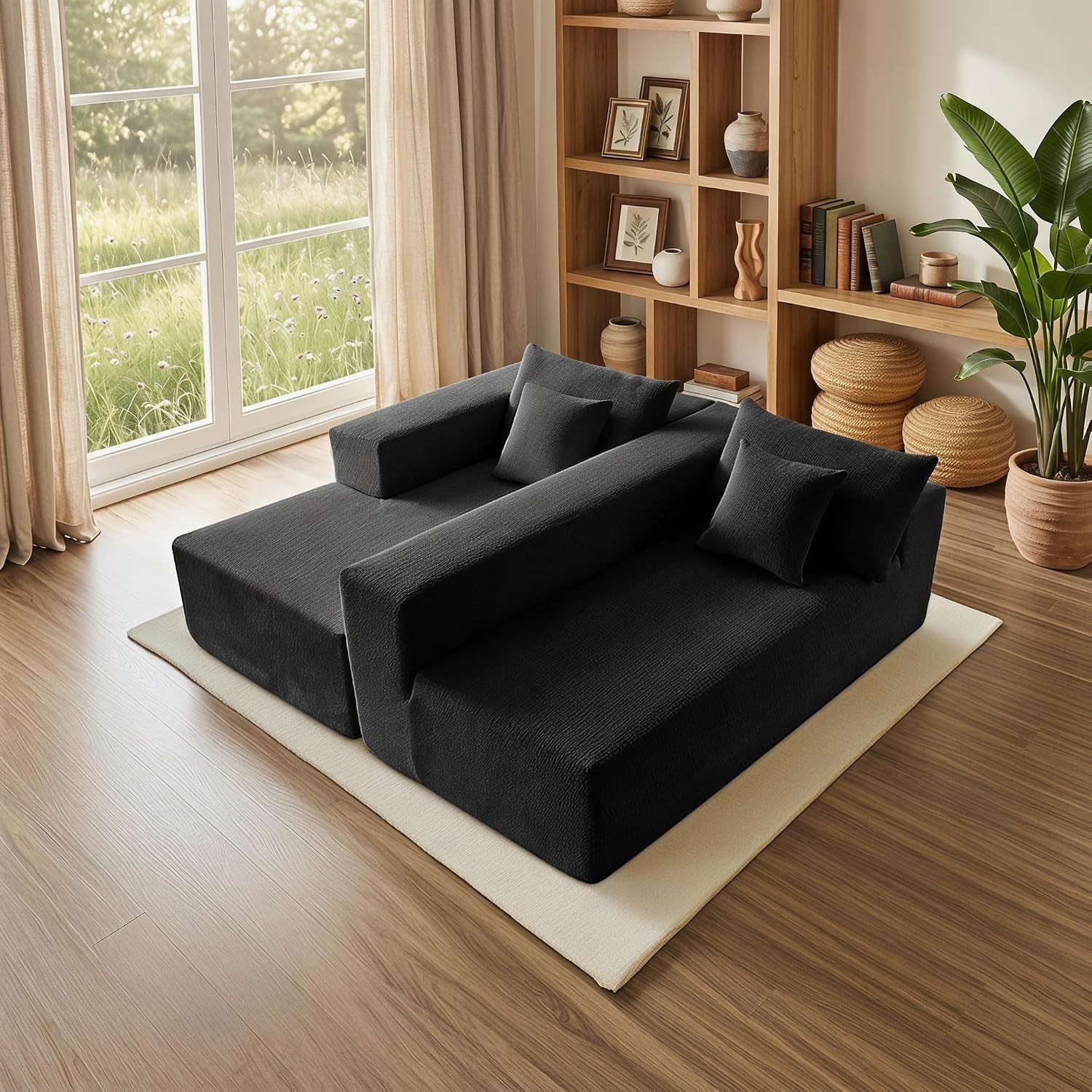 Top-down view of two black modular sofa pieces placed side-by-side on a pale rug by a large window and wooden shelving.