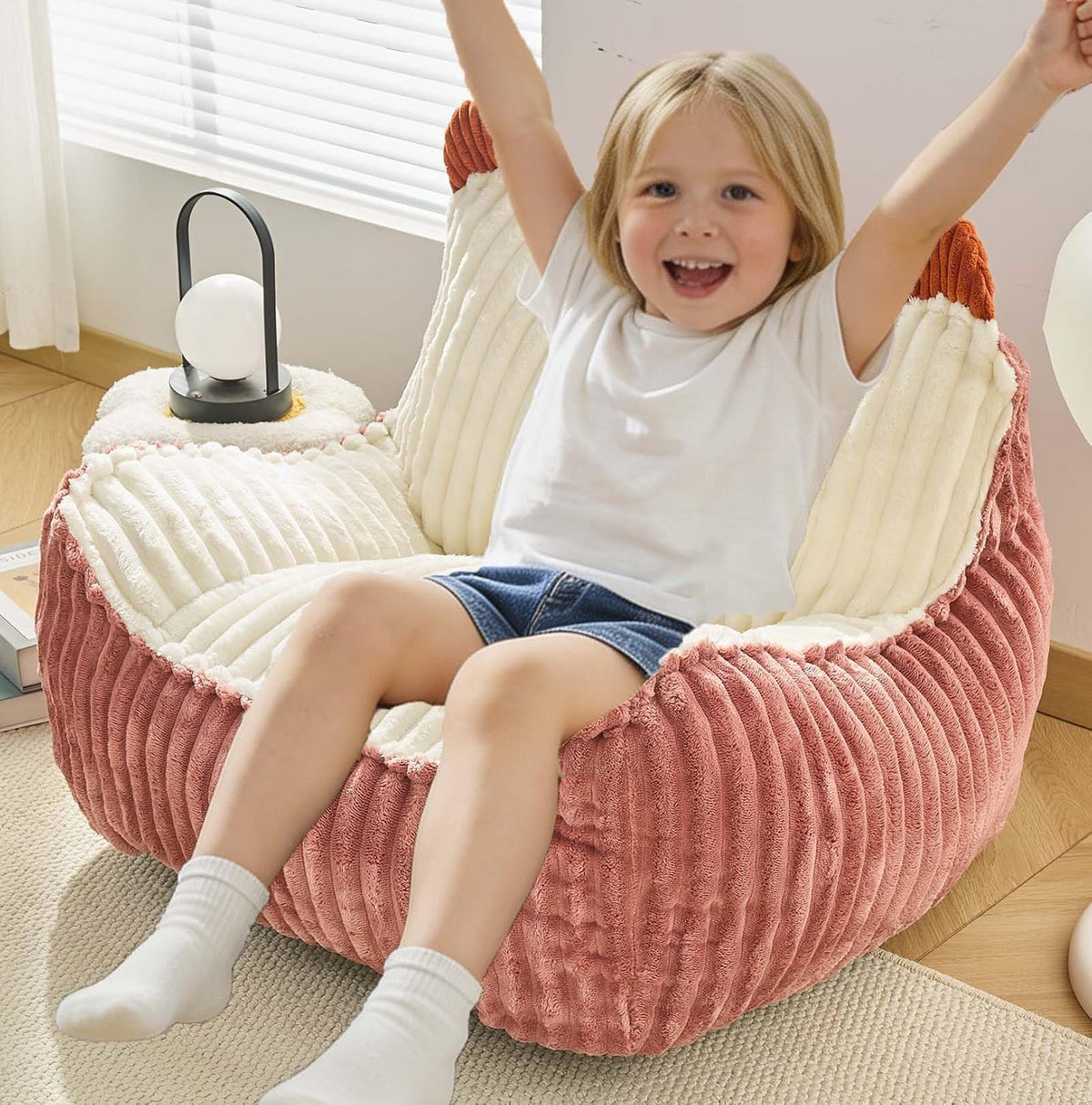 Small child cheering while seated in a two-tone pink and cream corded round bean bag chair in a bright room