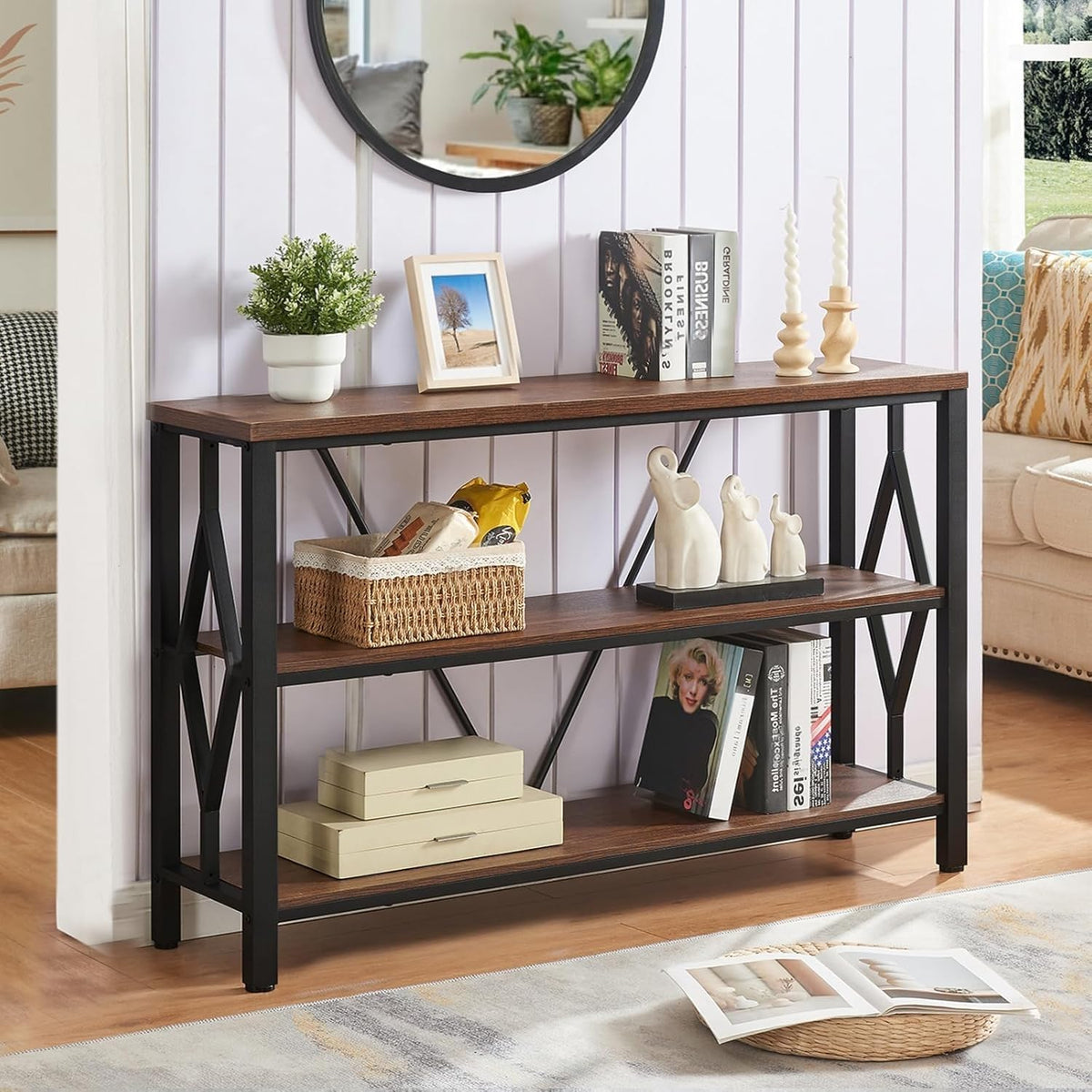 Front view of the rustic brown three-tier console against a pale paneled wall with mirror above.