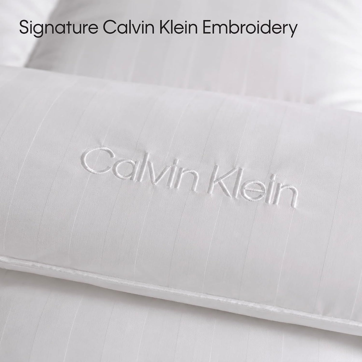 Tight crop of raised white embroidery on a striped comforter surface, focusing on the stitched lettering