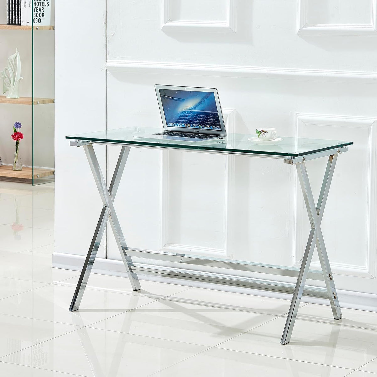Clear glass top desk in a white room setting, angled front-left view highlighting chrome X-shaped legs