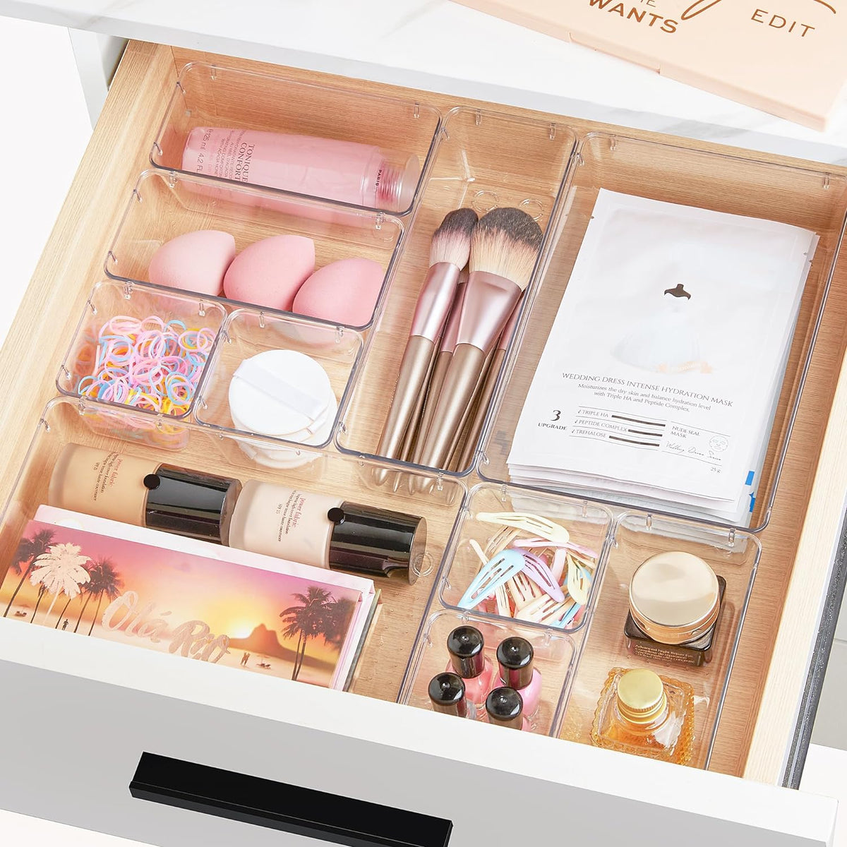 Open wooden drawer filled with clear organizers holding brushes, sponges, bottles and masks