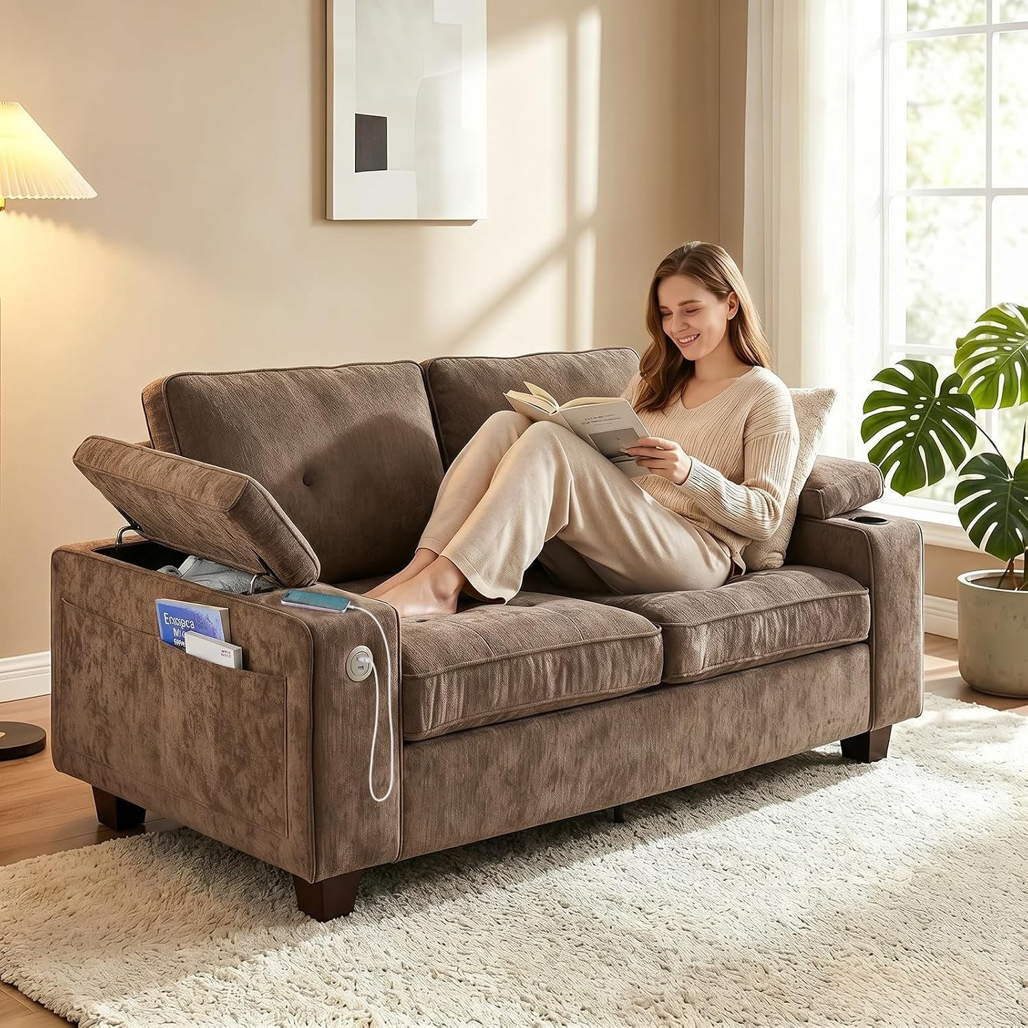 Side view of a brown loveseat with the left armrest open to show storage, cup holder on right arm, and a woman reading.