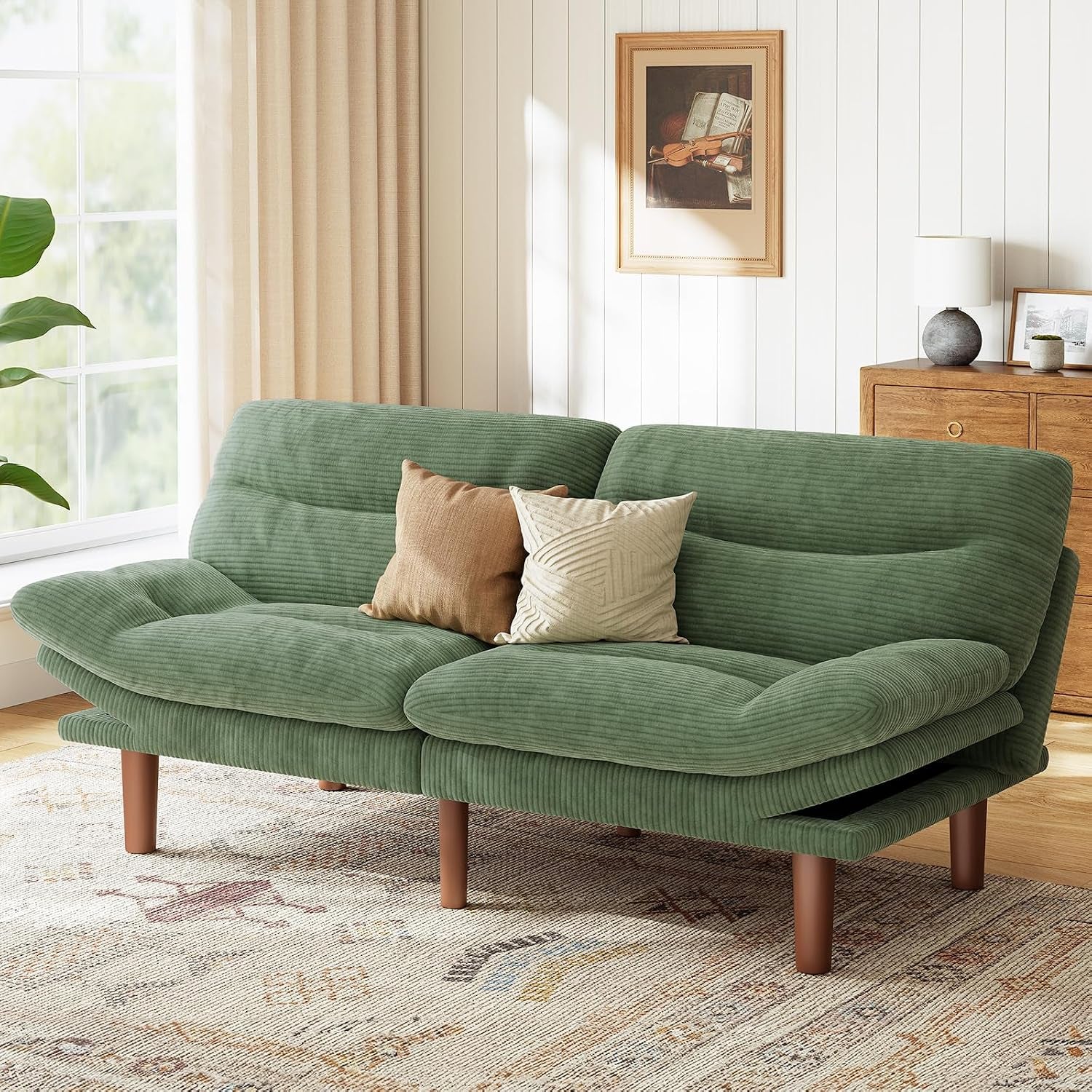 Green corduroy futon loveseat staged with two throw pillows on a patterned rug