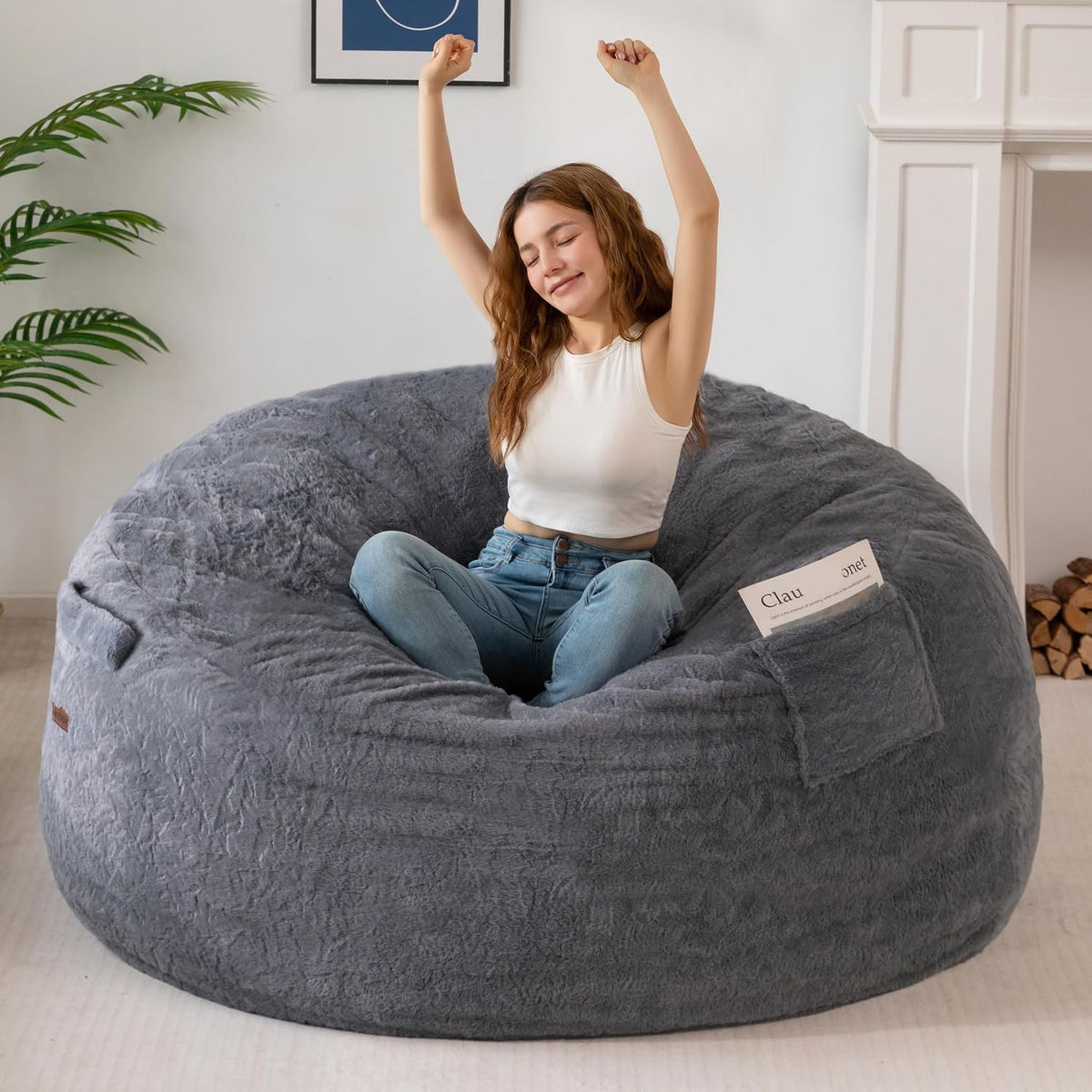 Young woman stretching with arms raised while seated cross‑legged in a large gray faux‑fur bean bag.