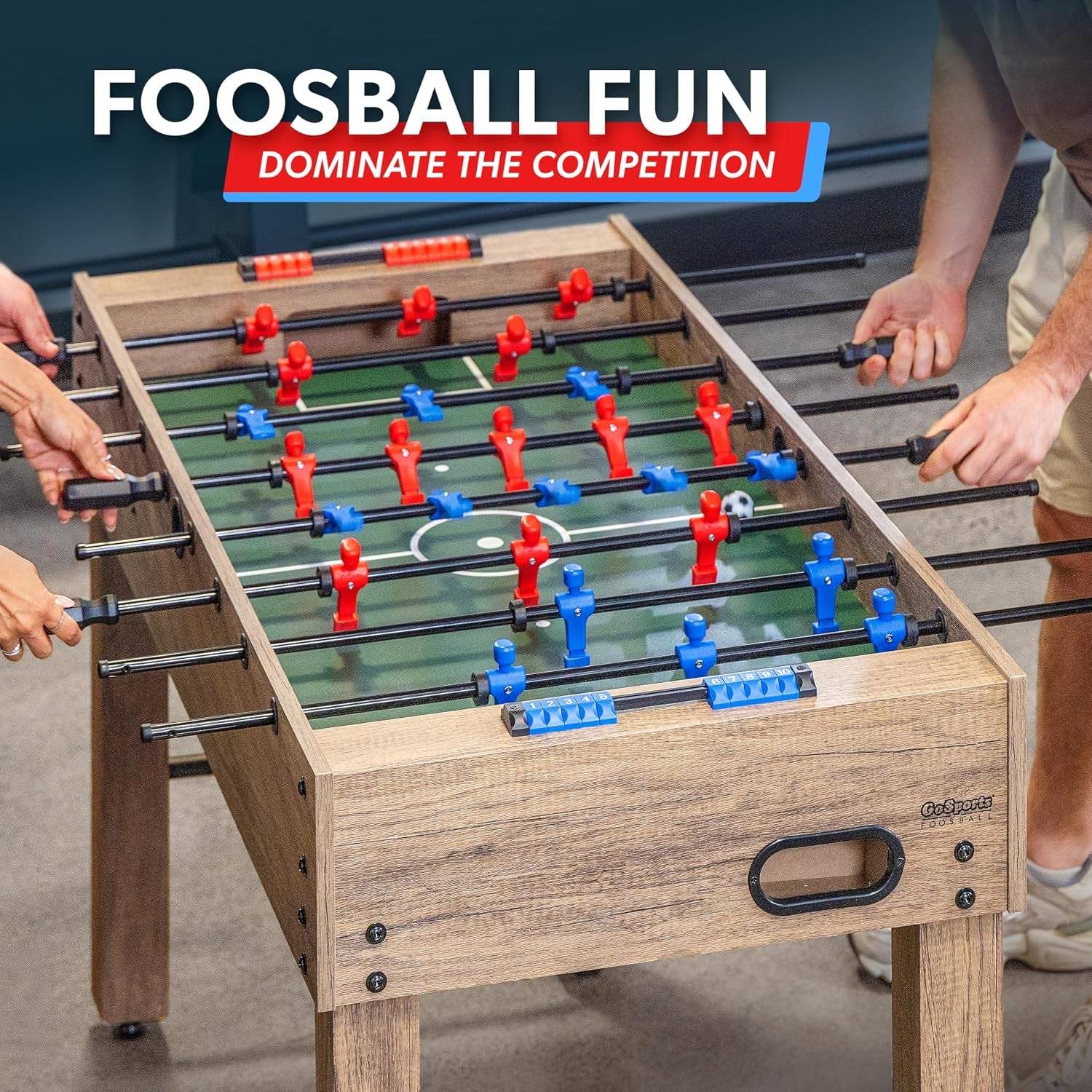 Top-down action shot of foosball table with players' hands on handles and a green low-friction playing field