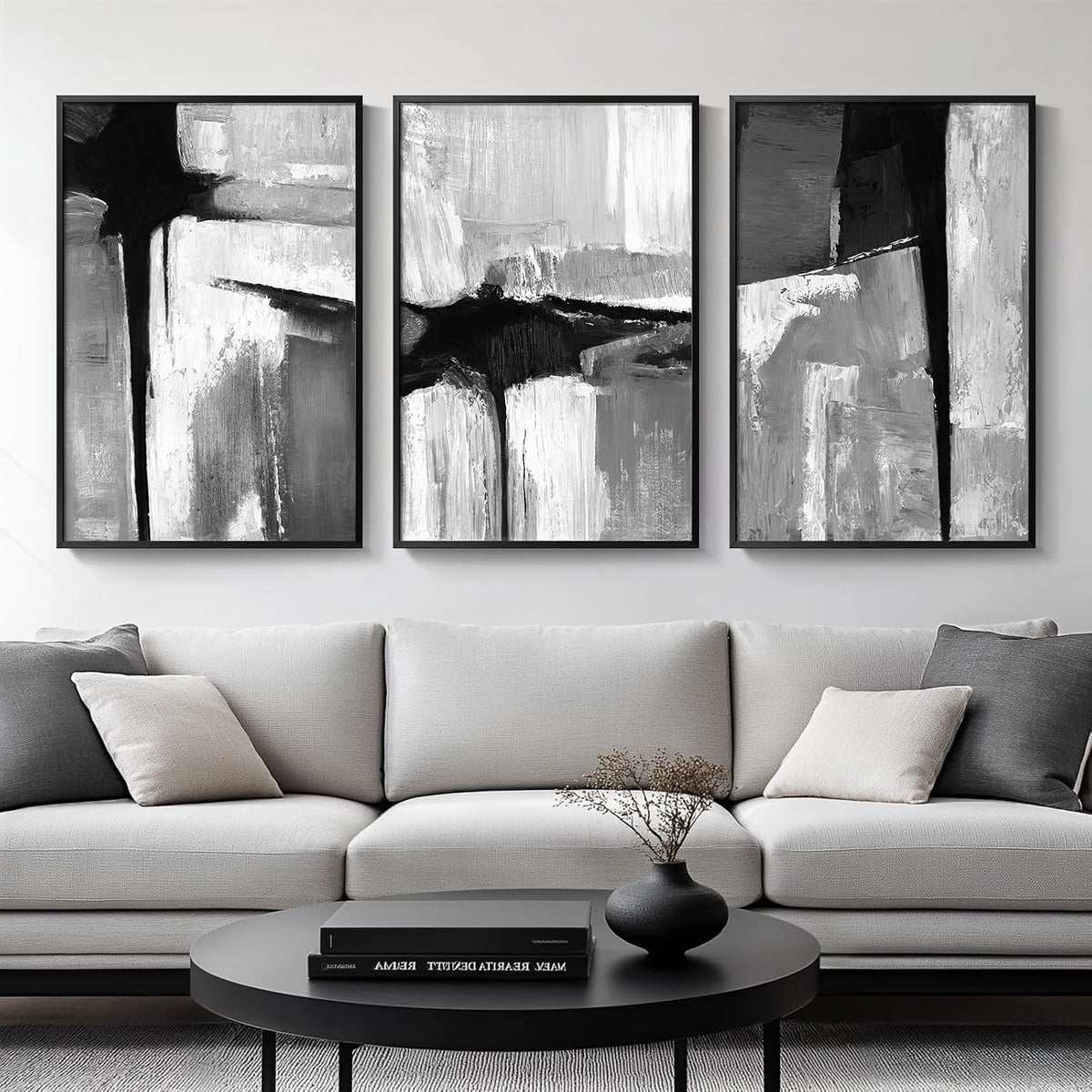 Three black-and-white gestural abstract panels in thin black frames mounted over a light gray sofa and round coffee table.