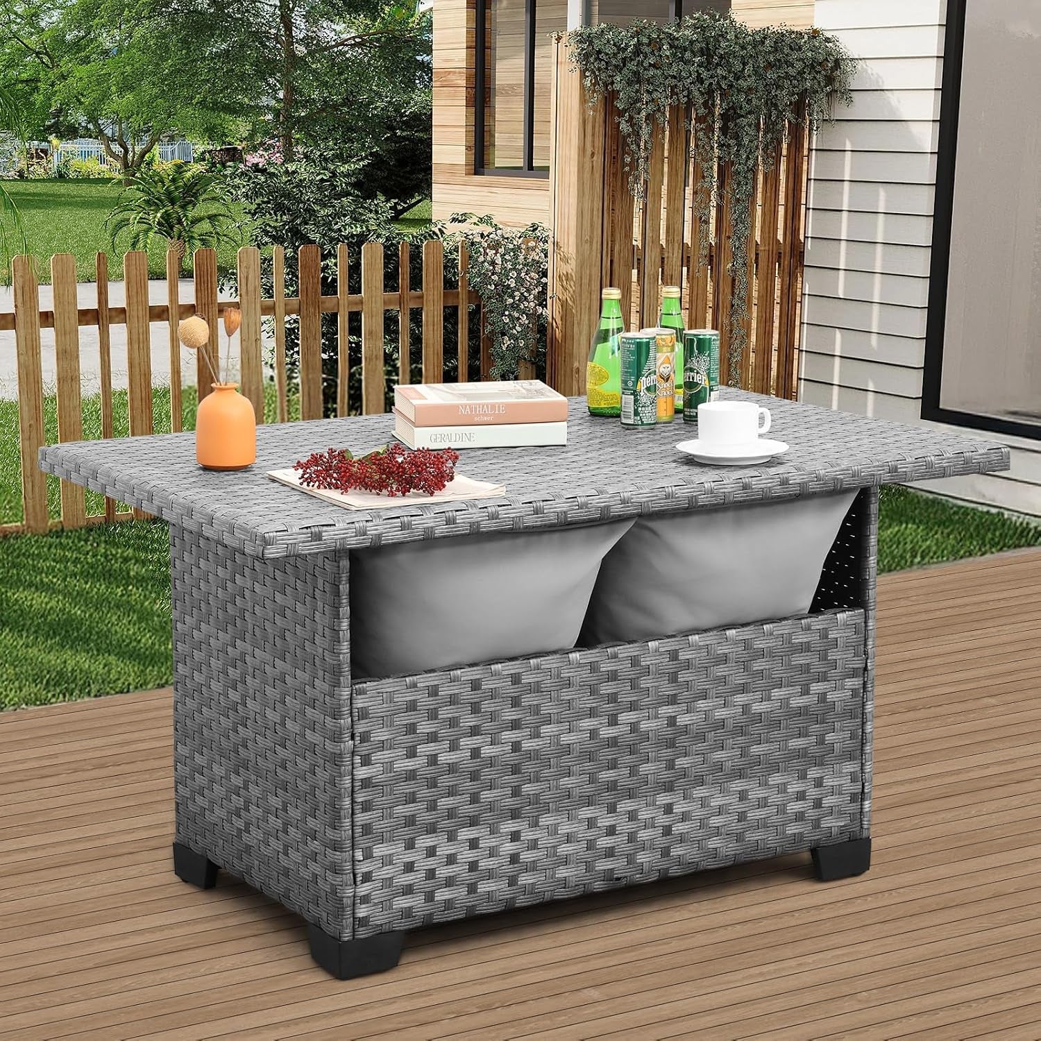 Grey wicker patio storage table placed on a wooden deck with a picket fence and greenery in the background