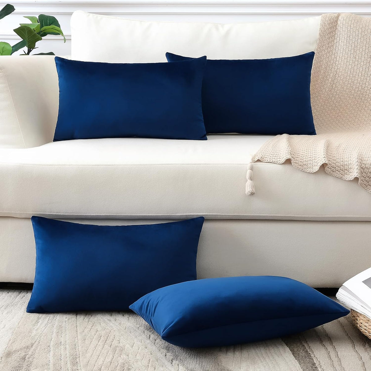 Two rectangular deep navy pillow covers on a cream sofa and matching pillows on the floor