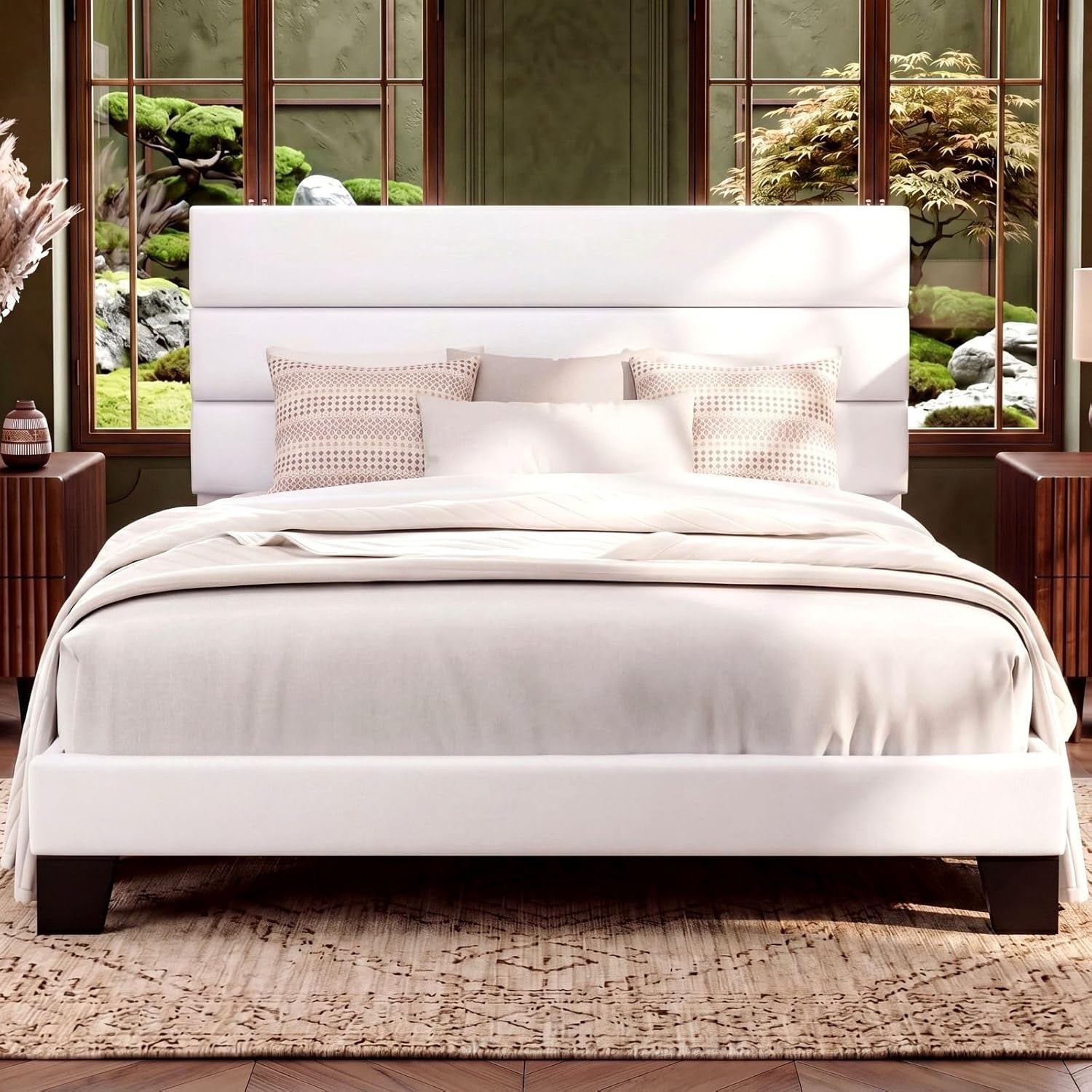 Front bedroom view of a white upholstered bed before wood-framed windows and a garden.