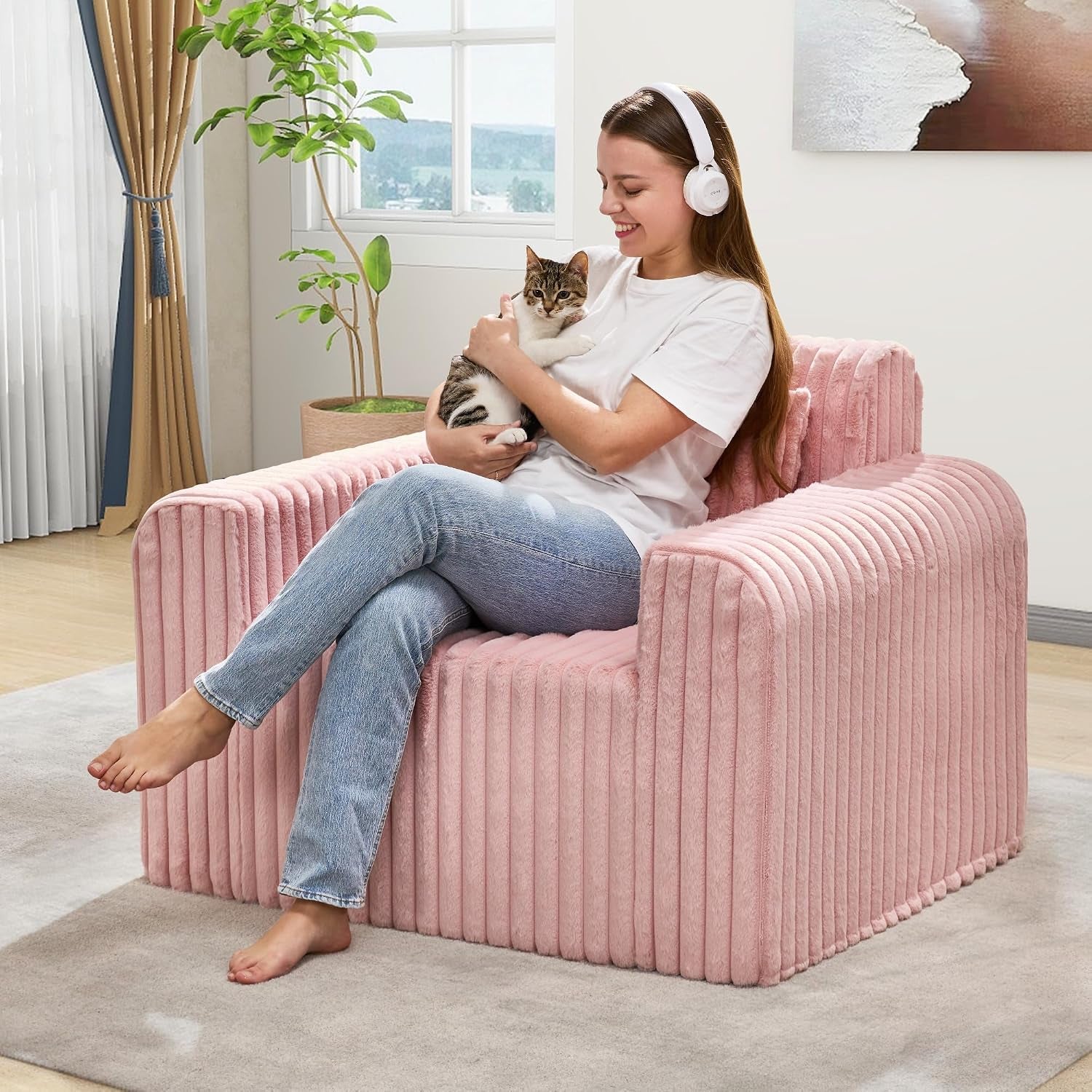Woman cradles a cat while seated on a pink ribbed floor chair in a sunny room.