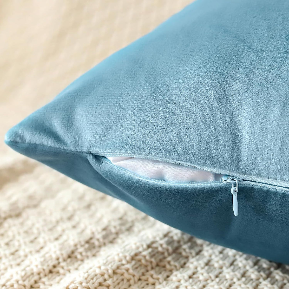 Close-up of a light blue velvet pillow cover showing a partially open zipper and fabric texture over a cream knit surface