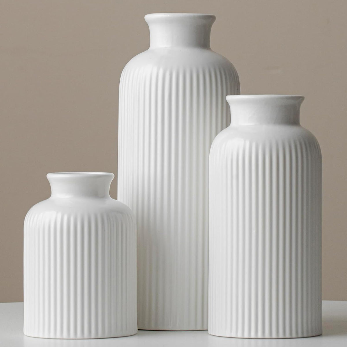 Three glossy white ribbed ceramic vases grouped against a beige backdrop