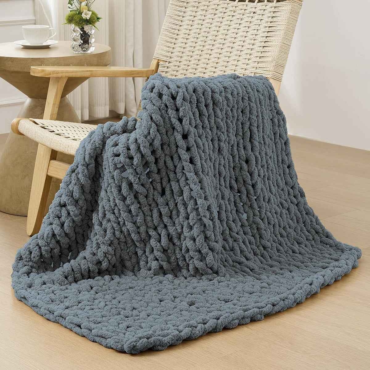 Dark-gray chunky knit throw casually draped over a woven wooden chair on a wood floor.