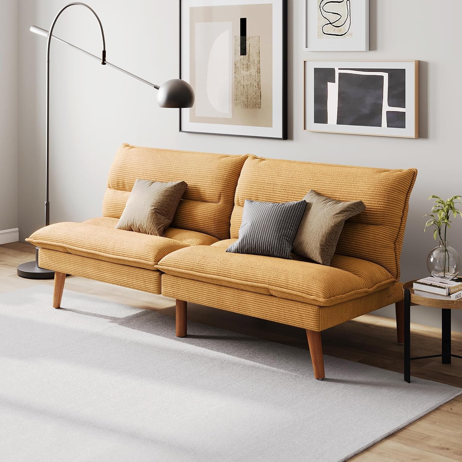 Mustard-yellow corduroy futon loveseat with throw pillows under wall art and a floor lamp.