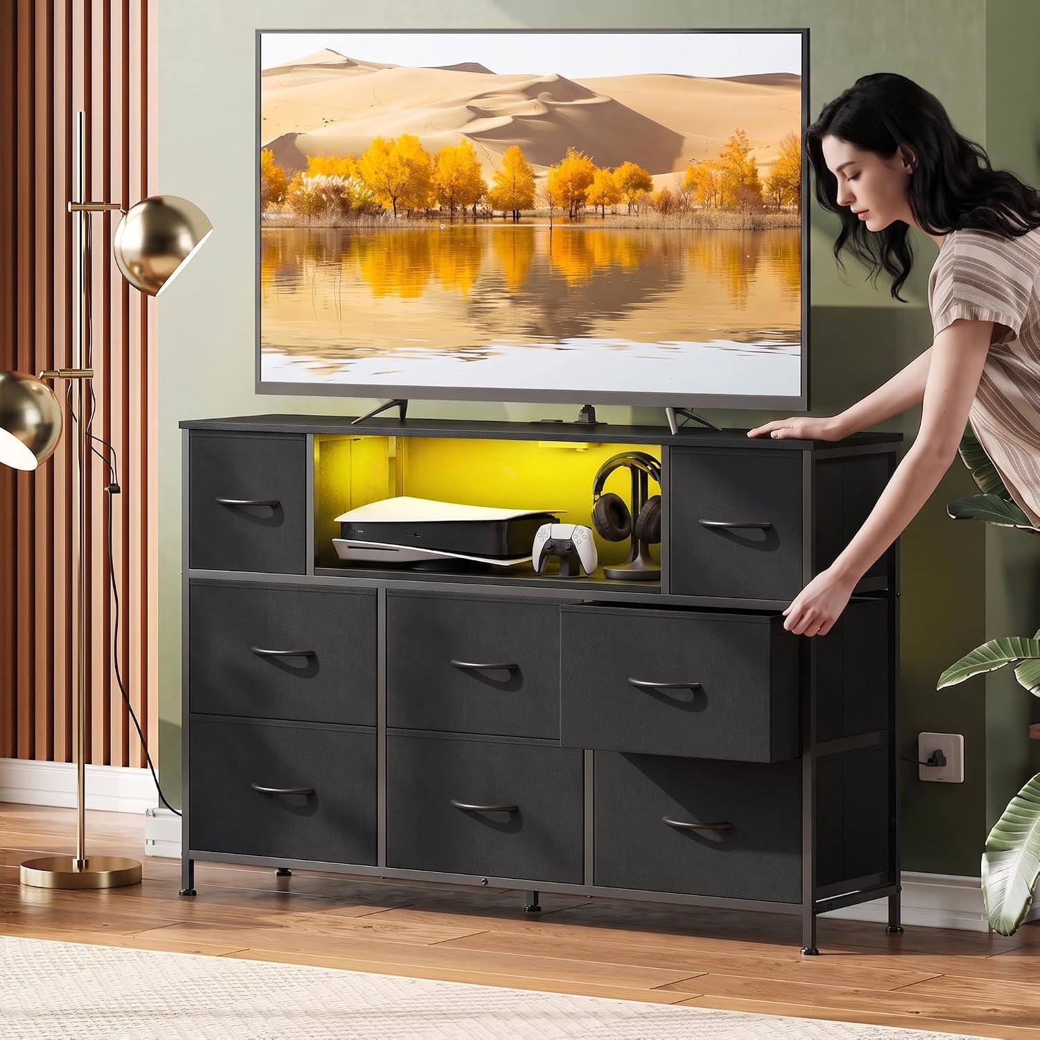 Black dresser in living room setting with open shelf lit yellow and woman opening a drawer