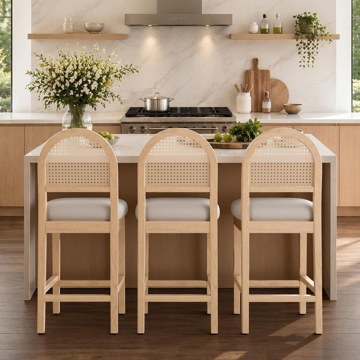 Rear-facing view of three light-wood rattan-back counter stools at an island, white cushions visible.