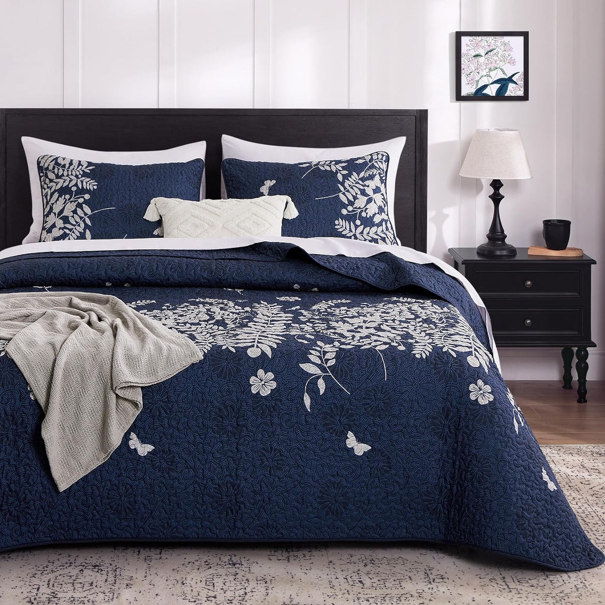 Navy blue floral quilt and matching pillow shams on a made bed with headboard and nightstand, front view
