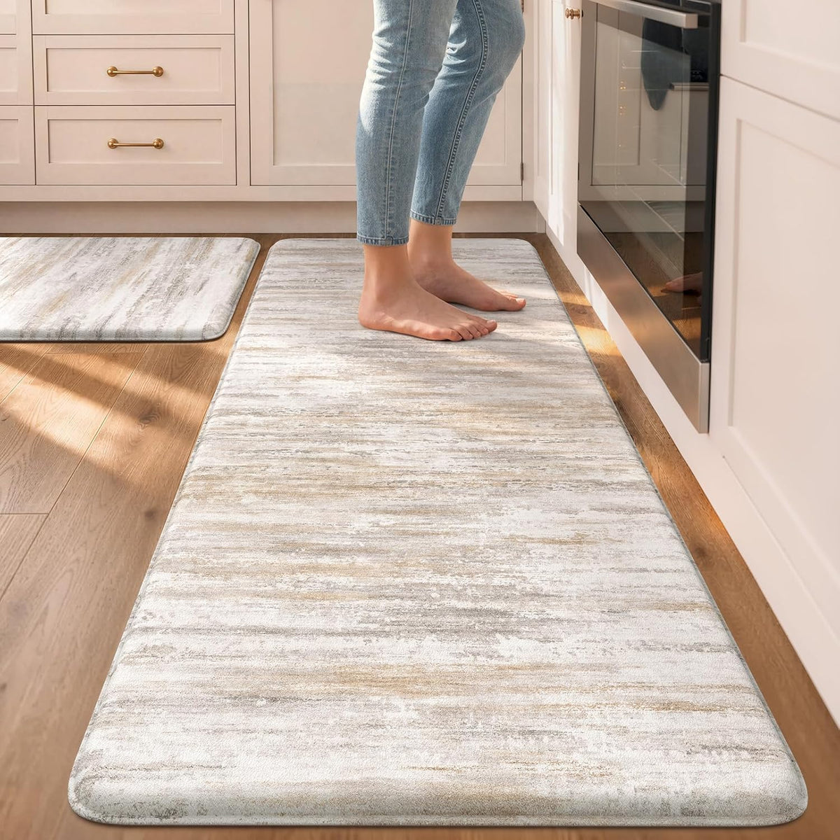 Close view of a beige abstract anti-fatigue mat under bare feet next to an oven.
