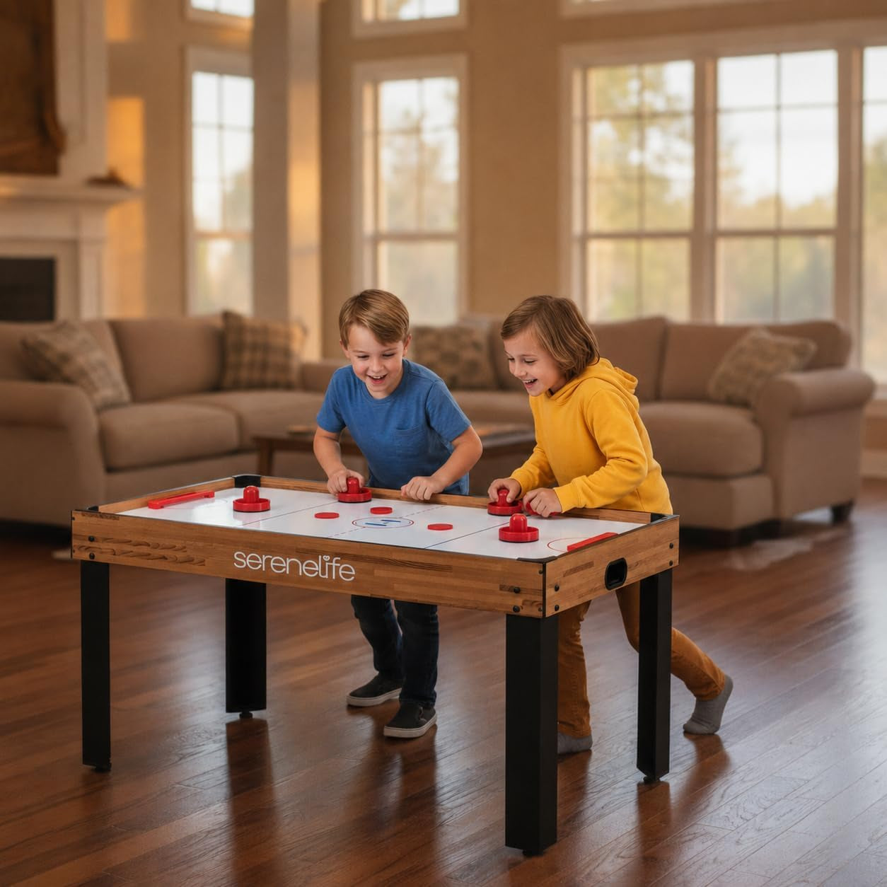 Two children lean over a tabletop air-hockey surface playing with red pushers in a cozy living room setting.