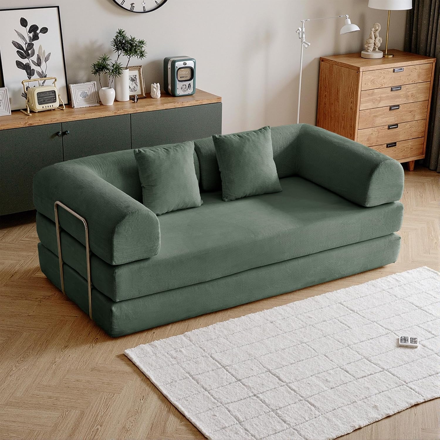 Angled view of a sage green corduroy folding sofa with three cushions and metal side rails