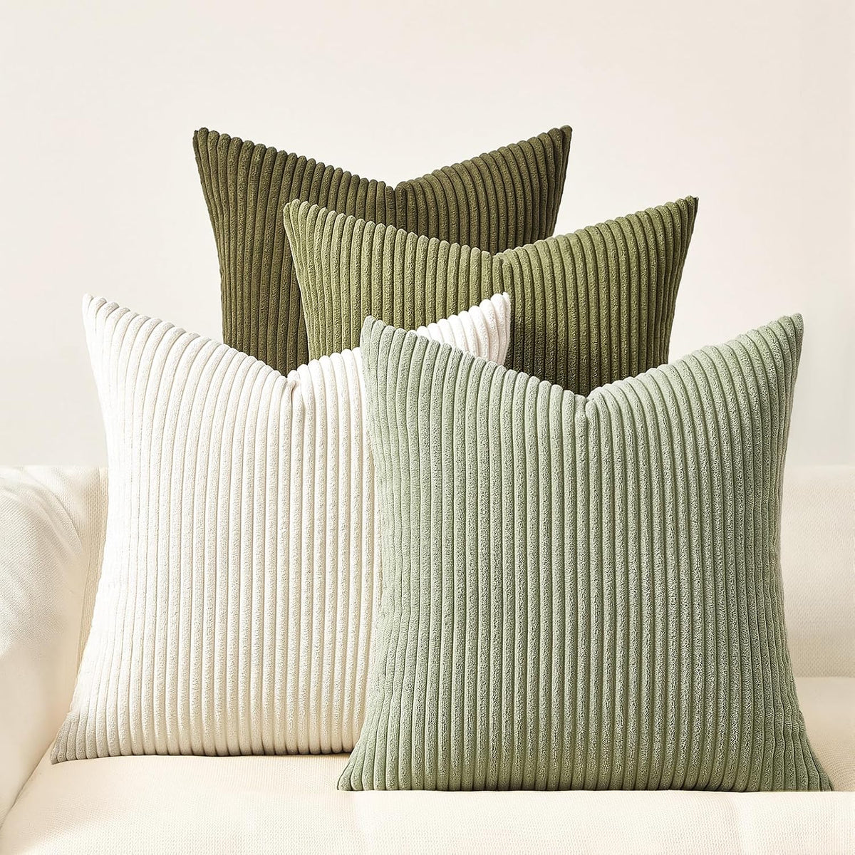 Three ribbed corduroy square pillows in olive, light green and off-white on a cream sofa