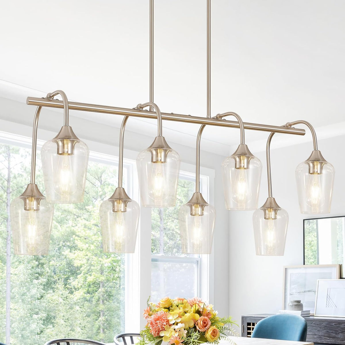 Linear six-light pendant in a warm nickel finish hanging over a dining table with floral centerpiece.