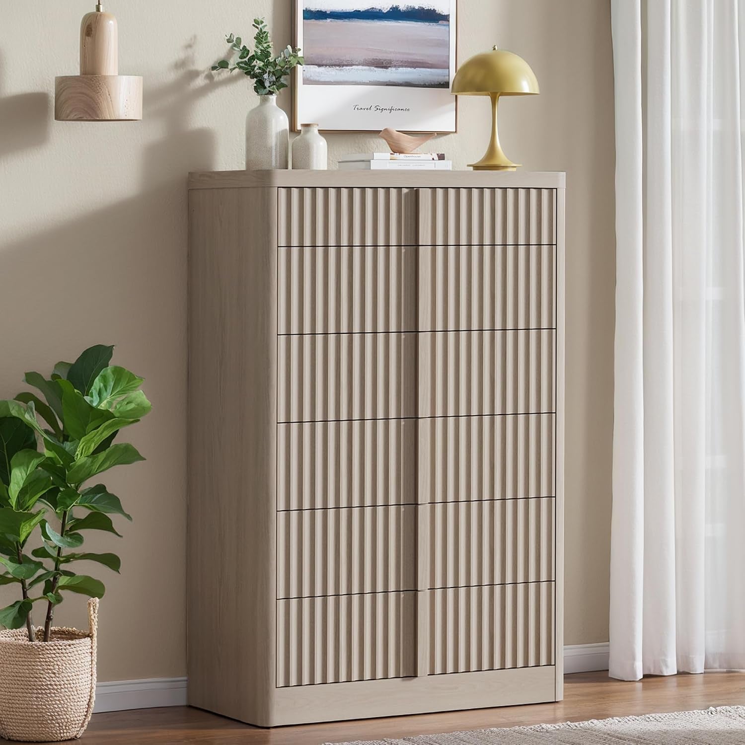 Tall fluted chest in a light beige finish staged in a living space with plant, artwork, and table lamp.