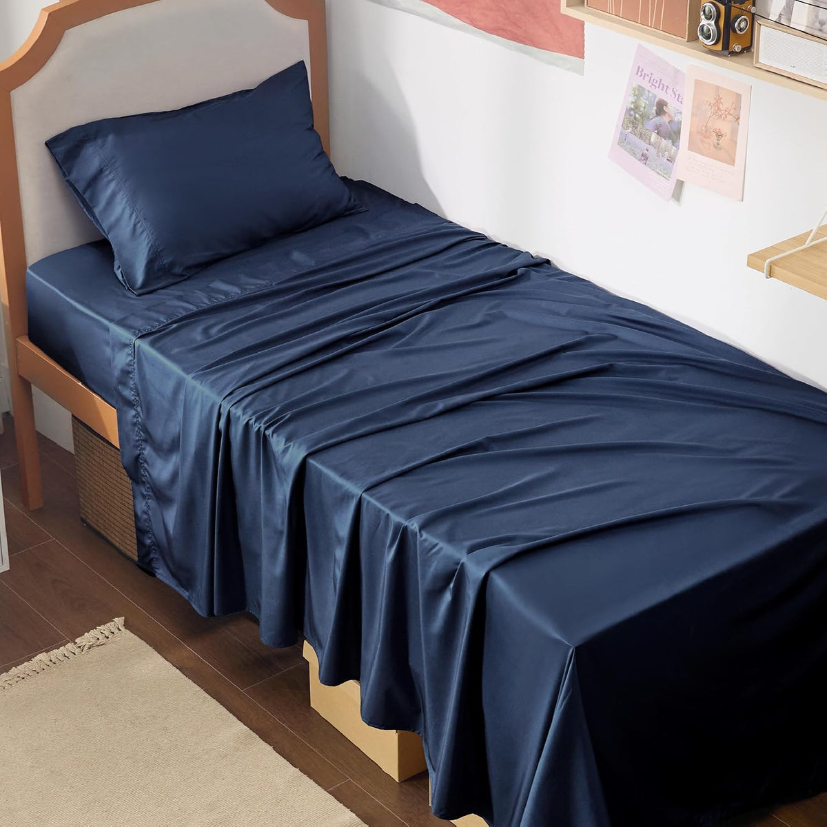 Angled view of a single bed dressed in deep navy sheets and a matching pillow with fabric draping to the floor.