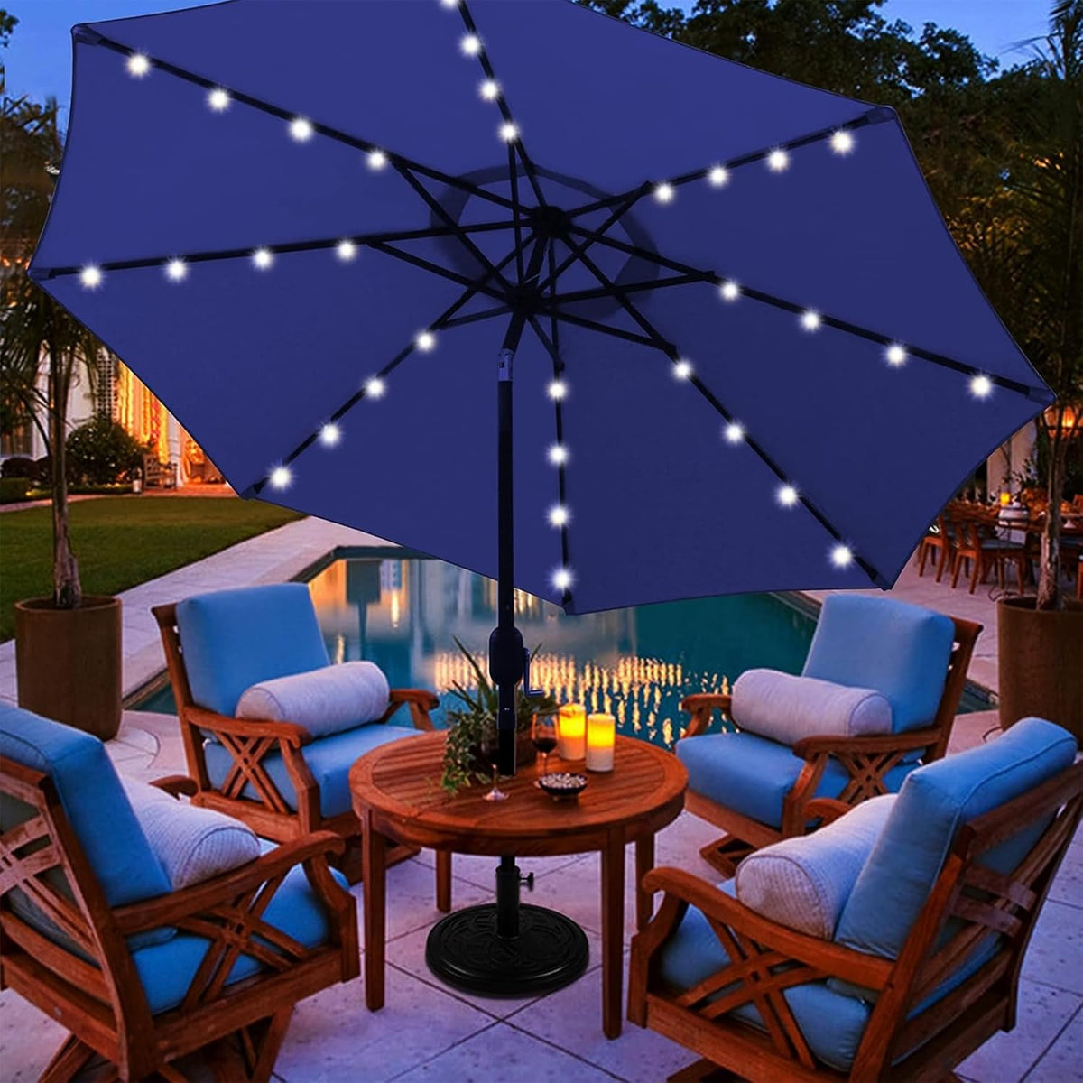 Close patio view of a blue umbrella with LED lights above a round wooden table and cushioned chairs by a pool.