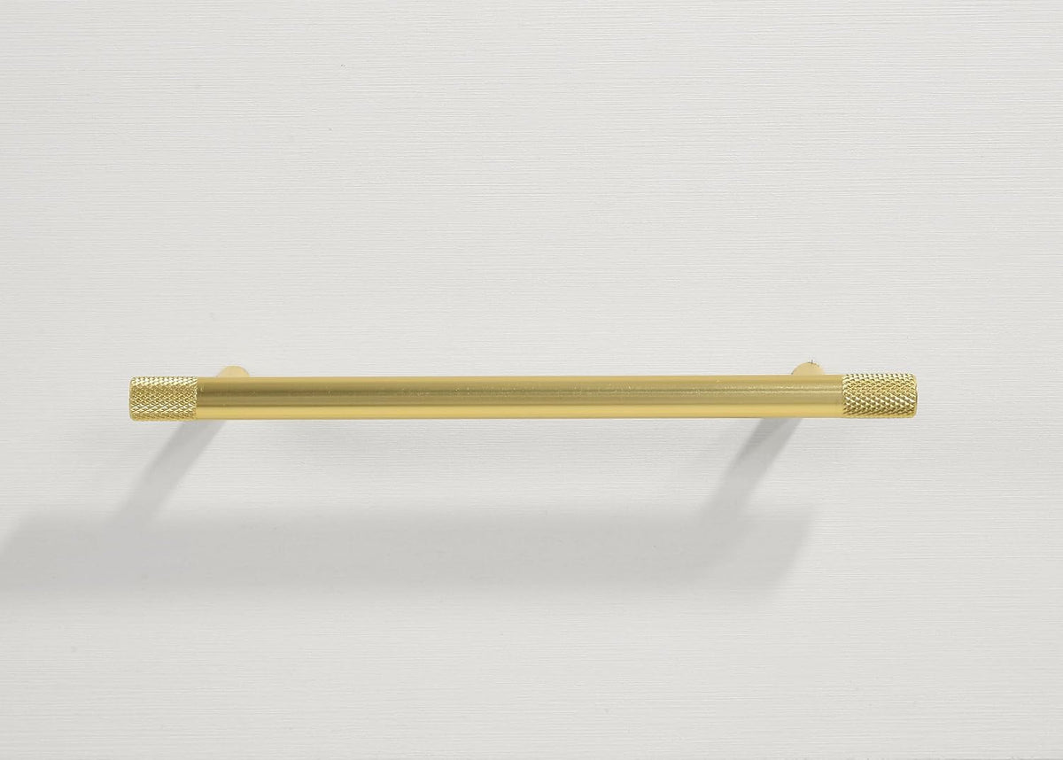 Close detail of a cylindrical gold drawer pull with knurled end caps on a textured white drawer front
